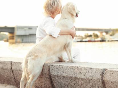 Une femme et son Golden Retriver en train de regarder au loin depuis le bord d'une rivière