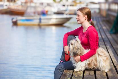 Un Shih Tzu sur un quai au bord d'un lac, à côté de sa maîtresse