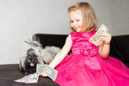 Une petite fille mettant des billets devant un Shih Tzu allongé sur un canapé