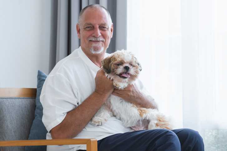 Un homme assis sur un fauteuil et portant un Shih Tzu dans ses bras 