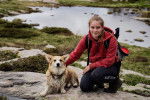 Un Welsh Corgi Pembroke allongé sur une montagne à côté d'une femme accroupie et portant un sac au dos 