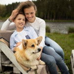 Un Welsh Corgi Pembroke allongé sur un banc en bois à côté d'une dame et d'un petit garçon