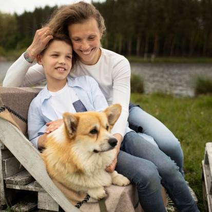 Un Welsh Corgi Pembroke allongé sur un banc en bois à côté d'une dame et d'un petit garçon