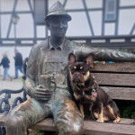 Un American French Bulldog assis sur un banc à côté d'une statut